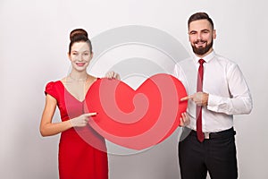 Handsome lively couple pointing finger at big heart, toothy smiling