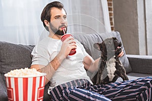 handsome loner palming bulldog and drinking beverage on sofa