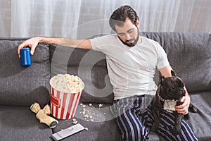 handsome loner sitting with bulldog on sofa and holding drink in living