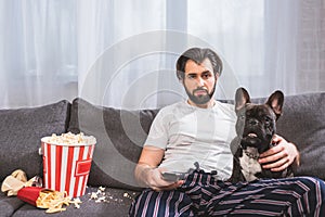 handsome loner watching tv with bulldog on sofa in living