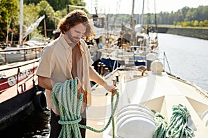 Handsome long haired man standing on boat in dock and holding line