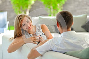 Handsome long haired young blonde woman sitting on a couch propped her head with one hand and holding a mug of delicious tea in an