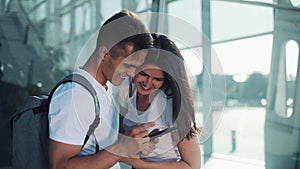 Handsome Lovely Couple standing near the Airport or Railway Station. They Pointing with her Finger in the Smartphone