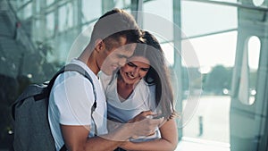 Handsome Lovely Couple standing near the Airport or Railway Station. They Pointing with her Finger in the Smartphone