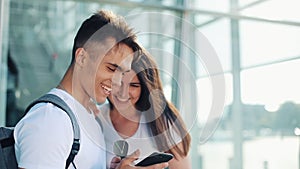 Handsome Lovely Couple standing near the Airport or Railway Station. They Pointing with her Finger in the Smartphone