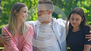 Handsome macho hugging best female friends during bench rest in park, rivalry