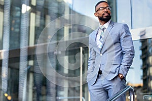 Handsome male african american business man CEO in a stylish chic suit at the workplace, standing confidently in front of financia