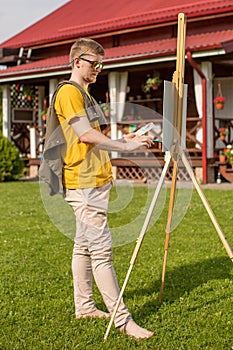 Handsome male artist painting picture on easel outside, summer inspiration