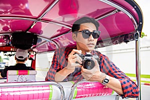 Handsome male Asian tourist holding camera on tuk tuk taxi in Bangkok Thailand
