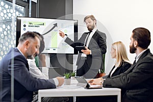 Handsome male bearded chief, having a meeting together with his focused international colleagues, and showing business