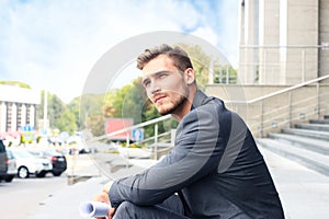 Handsome male business executive sitting on stairs outside a building.