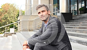 Handsome male business executive sitting on stairs outside a building.