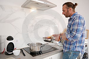 Handsome male chef cooking in the home kitchen, mixing tomato sauce while preparing Italian meal