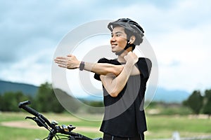 Handsome male cyclist doing stretching by his bicycle on road before workout with bike in nature