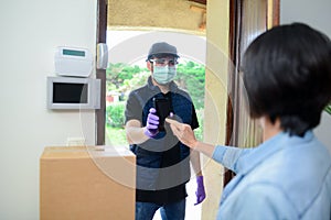 Handsome male delivery man delivering parcel to female client at home with mask against covid19 coronavirus virus infection