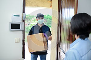 Handsome male delivery man delivering parcel to female client at home with mask against covid19 coronavirus virus infection