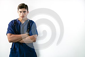 Handsome male doctor in blue scrubs with folded arms isolated against white backdrop