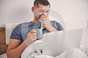 Handsome male is drinking tea and sneezing