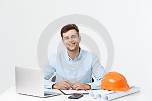 Handsome male engineer is using a notebook for work. He is sitting at the desk and smiling. Copy space on side.