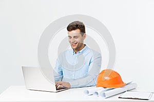 Handsome male engineer is using a notebook for work. He is sitting at the desk and smiling. Copy space on side.