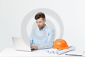 Handsome male engineer is using a notebook for work. He is sitting at the desk and smiling. Copy space on side.