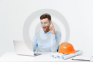 Handsome male engineer is using a notebook for work. He is sitting at the desk and smiling. Copy space on side.