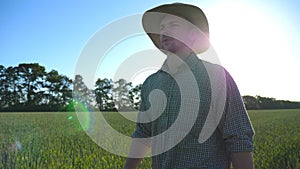 Handsome male farmer in hat walking over green wheat field on his farm. Young confident man going on cereal plantation