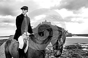 Handsome Male Horse Rider riding horse on beach in traditional fashion with St Michael`s Mount in background