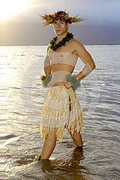 Handsome male hula dancer stands in the water as the sun sets.