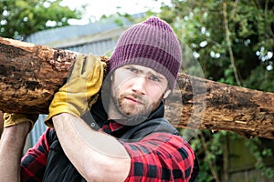 Handsome male lumberjack carries wood log on his shoulder