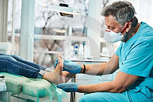 Handsome male in medical mask and gloves doing feet massage after pedicure