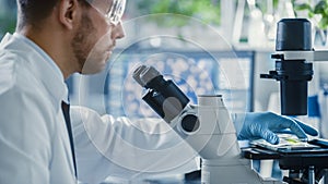 Handsome Male Microbiologist Putting Green Leaf Sample under Microscope. Medical Scientist Working