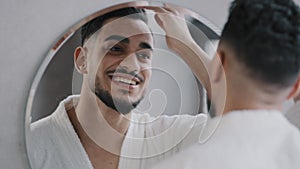 Handsome male model Indian hipster Arabian bearded guy doing hairstyle correct hair looking in mirror reflection