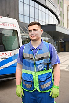 Handsome male paramedic stands near a modern building near ambulance