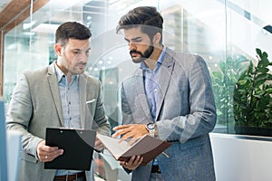 Handsome male partners discussing paperwork while standing in office lobby.