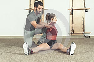 Handsome male personal trainer with a beard helping young fitness girl to stretch her muscles after hard training workout, selecti