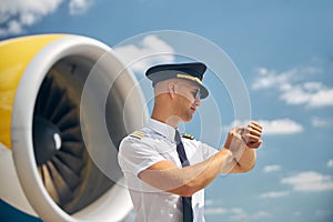 Handsome male pilot looking at wristwatch at airfield