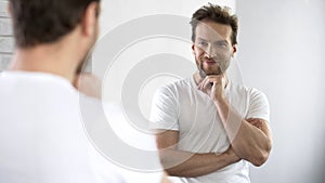 Handsome male posing at mirror, feeling happy and cheerful, satisfied with life