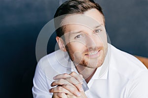 Handsome male, positive smile, hands together, successful in business, white shirt. Isolated on dark background. Emotions concept