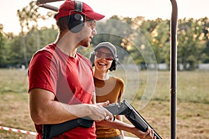 Handsome male shooting instructor teaches excited lady how to handle weapon