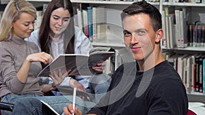 Handsome male student smiling to the camera, while doing homework at library