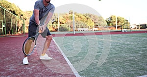 Handsome male tennis player hitting tennis ball with racket outdoors on tennis court