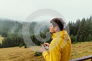 Handsome male tourist in a yellow jacket with a plate in his hands stands on the terrace of a country house in the mountains and