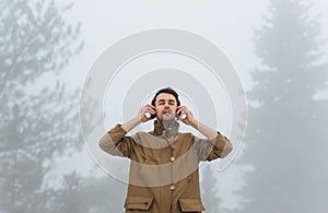 Handsome male walking in misty nature, listening to music on his headphones outside with copy space for text. Traveler man wearing