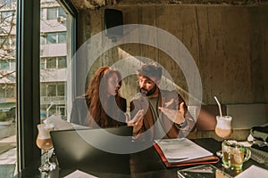 Handsome male worker trying to explain something to his redhead female colleague. She looks scared cause he raised his