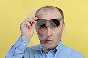 A handsome man 45-55 years old on a yellow background holds glasses in his hand.