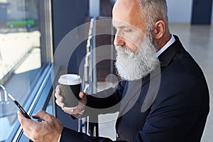 Handsome man age of 50-60 holding cup of coffee and surfing in p