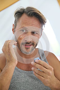 Handsome man applying anti-aging cream on