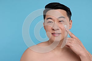 Handsome man applying cream onto his face on light blue background. Space for text