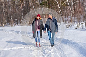 Handsome man and attractive young woman walking along snowy country road in sunny day. Beautiful look, male and female fashion,